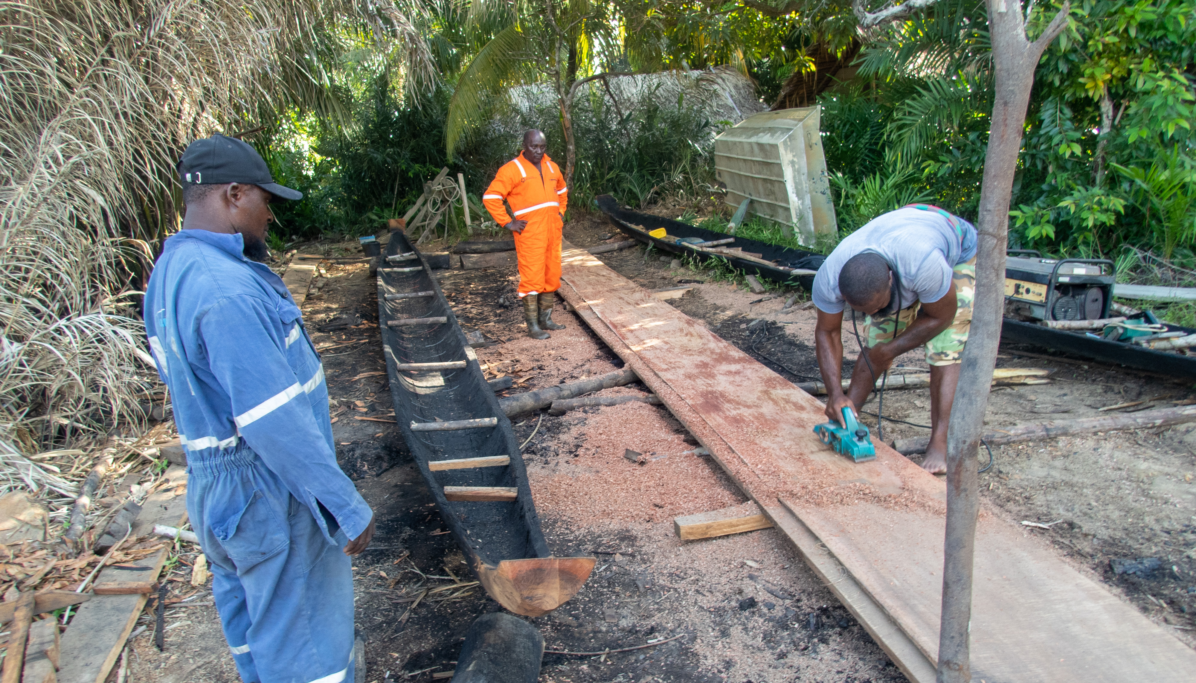 Building canoes. The hull is constructed from a single hollowed out log, on the left. The sides are built from solid slabs of timber being planed by Javeh on the right.