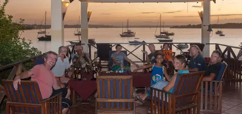 Tanga Yacht Club at Sunset. Around the circle starting far left: Das, Roy, Happy, CB, Terry, Malaika, Arthur, Gerhard, Karina and the irrepressible Marina. Anjea is just visible to the right of the bell.