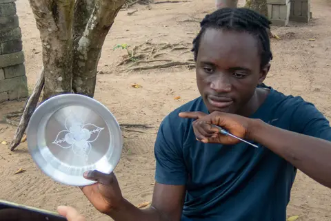 Young man carving an aluminium plate. His only tools are a pencil and a sharpened screwdriver.